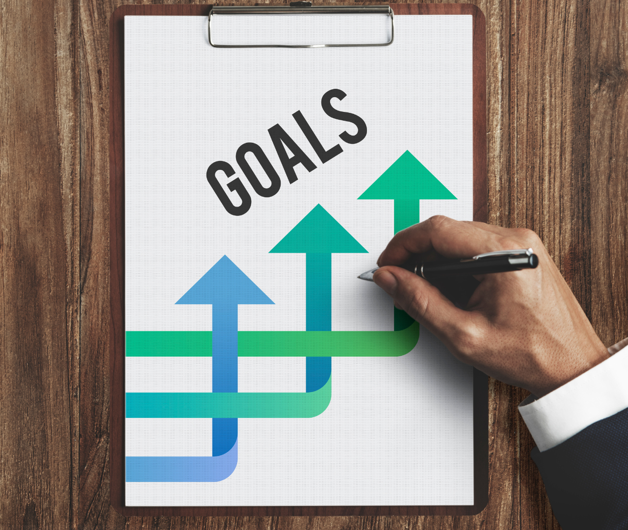 Hand drawing upward arrows on a clipboard labeled "Goals," symbolizing the importance of proven outcomes in SEO services, including case studies, improved rankings, and increased organic traffic, showcasing the company's ability to achieve significant results.