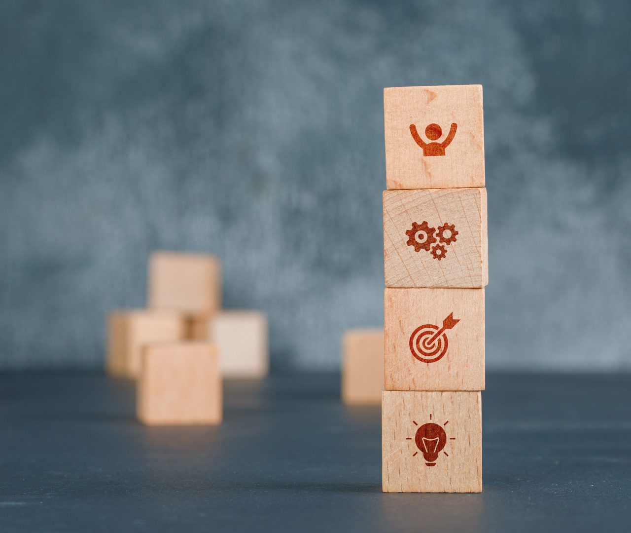 Wooden blocks stacked with icons representing success, gears, target, and idea, symbolizing the importance of ethical conduct and best practices in SEO outsourcing to prioritize long-term outcomes over quick profits.