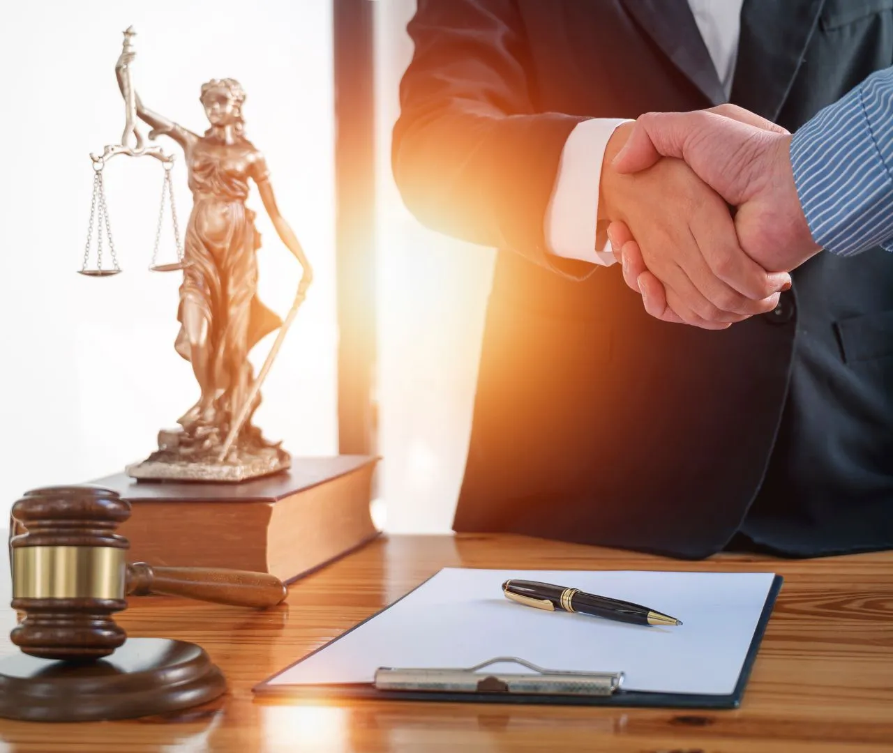 Two business professionals shaking hands with a statue of Lady Justice, a gavel, and legal documents on a desk, representing SEO strategies tailored for corporate law firms to enhance online visibility and establish authority in the legal industry.