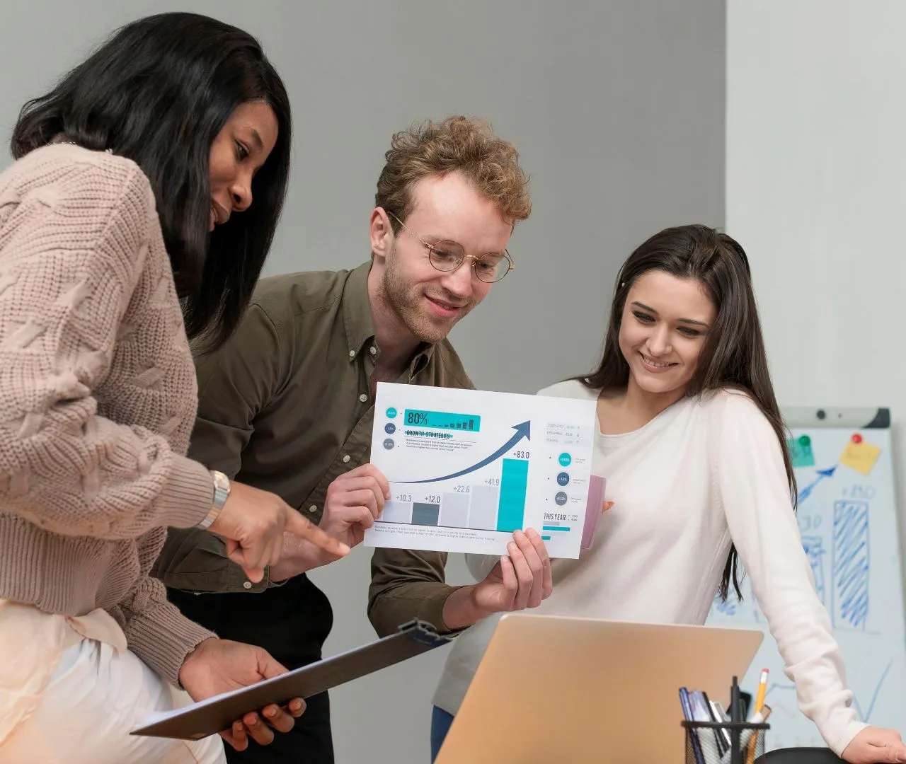 A group of three professionals analyzing graphs and charts on a laptop, representing the development of tailored SEO strategies for dentists based on industry-specific expertise.