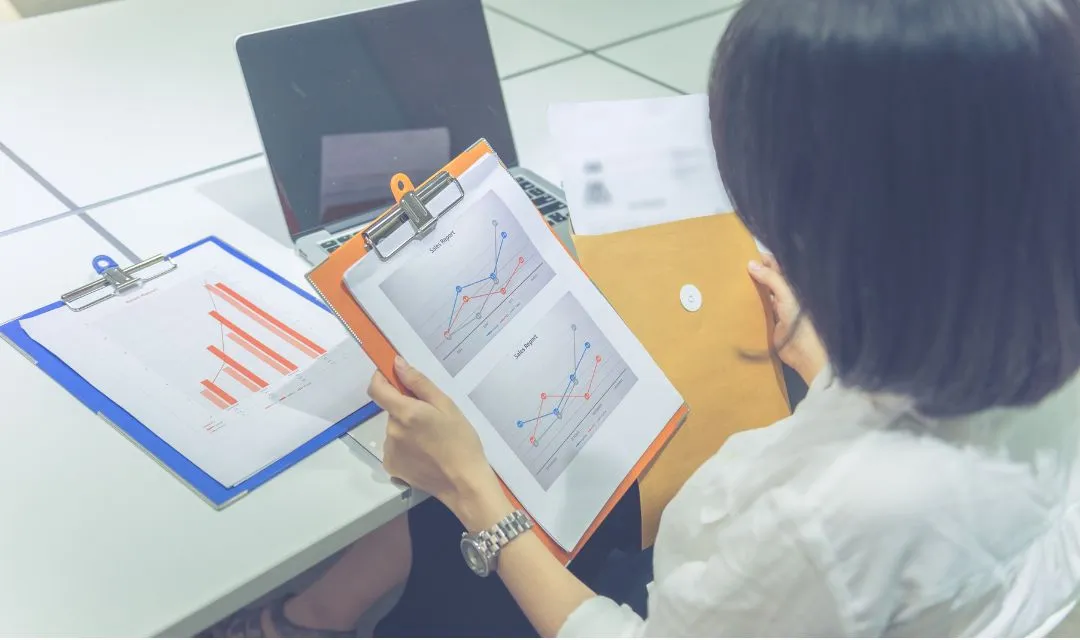 A person reviewing sales reports and graphs at a desk, symbolizing the impact of a successful SEO and reputation management strategy on improving online presence and patient appointments for a multi-location dental practice.