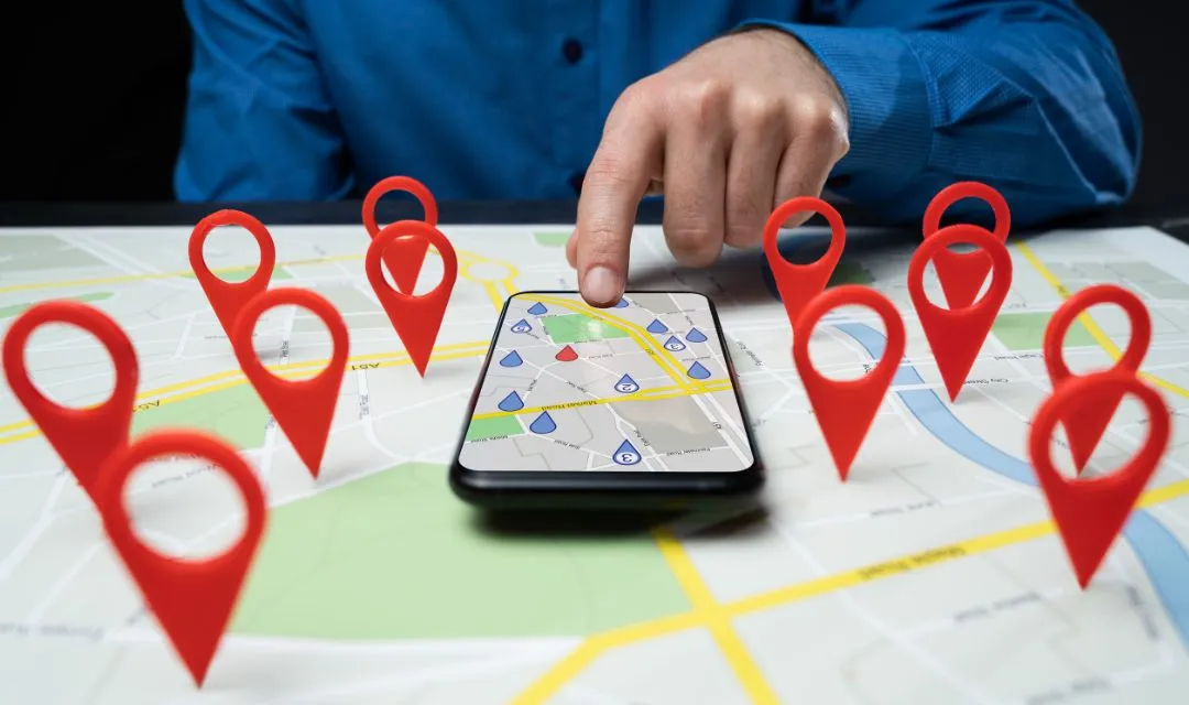 A person pointing at a smartphone displaying a map with red location pins, symbolizing the strategy of using local SEO to increase a dental clinic’s visibility and attract more local patients.