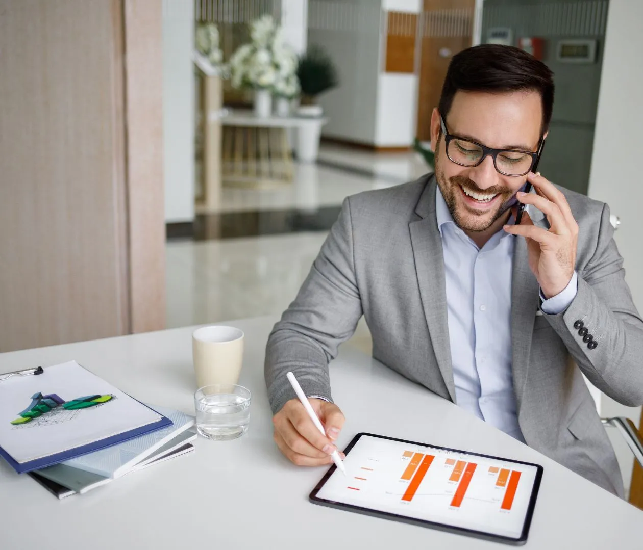 A smiling businessman talking on the phone while analyzing data on a tablet, representing increased visibility and higher rankings in search engine results through effective NetSuite SEO strategies.