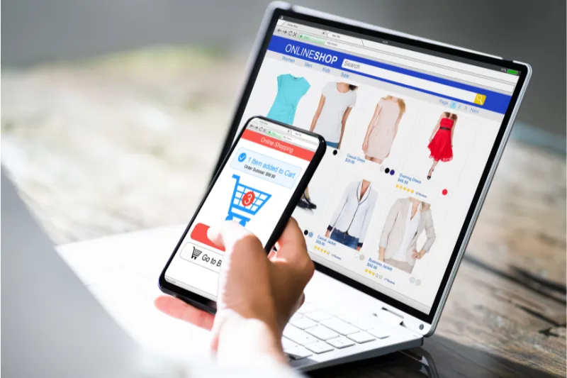 Person using a smartphone and laptop to browse an online clothing store, illustrating the need for SEO optimization on Netsuite for improved organic traffic and sales.